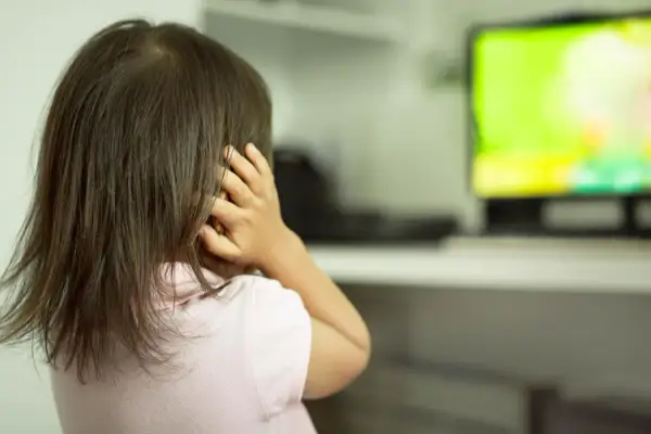 Dziewczynka z autyzmem zasłania uszy, reagując na bodźce. Ekran telewizora emituje jasne, intensywne kolory.