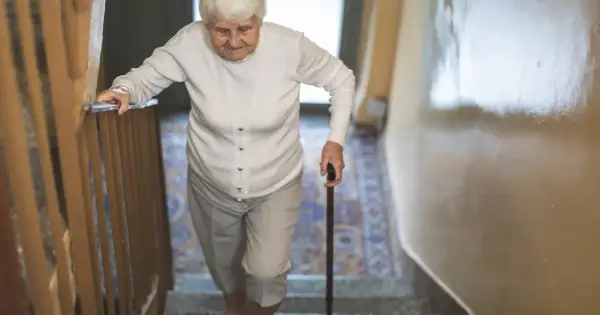 Starsza pani z laską wspina się po schodach, zmagając się z objawami parkinson w nogach.