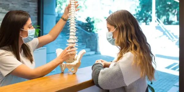 Fizjoterapeuta wyjaśnia pacjentce model kręgosłupa, omawiając, czy z przepukliną kręgosłupa można pracować.