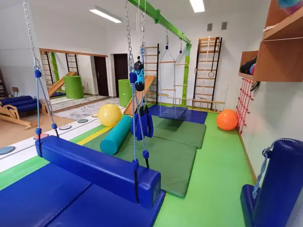 Sala do terapii integracji sensorycznej: huśtawki, drabinki, piłki i materace do ćwiczeń.