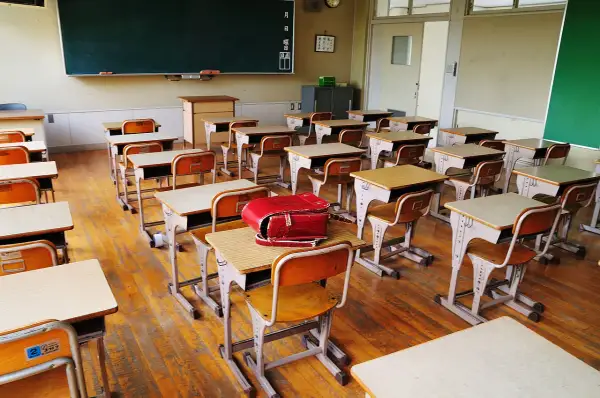 Pusta klasa z rzędami ławek i krzeseł, gotowa na lekcje w szkole dla dzieci z autyzmem. Czerwony tornister leży na jednej z ławek.