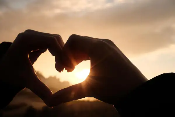 Dłonie tworzą serce na tle zachodzącego słońca. Początek pięknej historii, która może być jak love bombing.