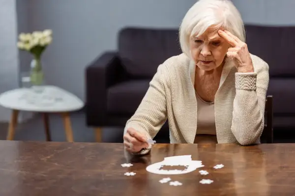 Starsza kobieta zmagająca się z układanką, symbolizującą wczesny alzheimer. Jej zamyślona twarz i gest wskazują na trudności z pamięcią.