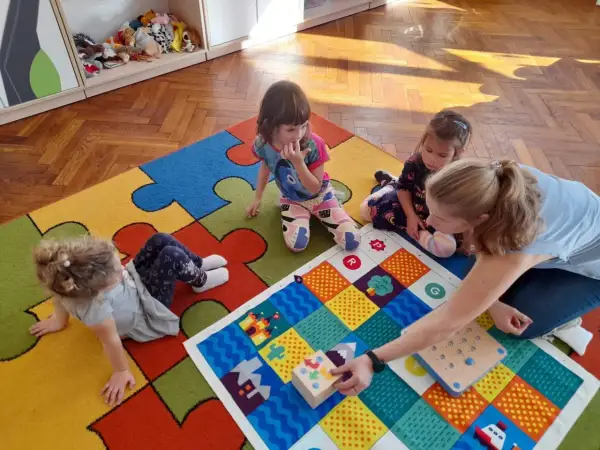 Wspólna zabawa w przedszkolu, gdzie dzieci z autyzmem uczą się przez interakcję. Kolorowa mata i pomoce dydaktyczne wspierają rozwój.